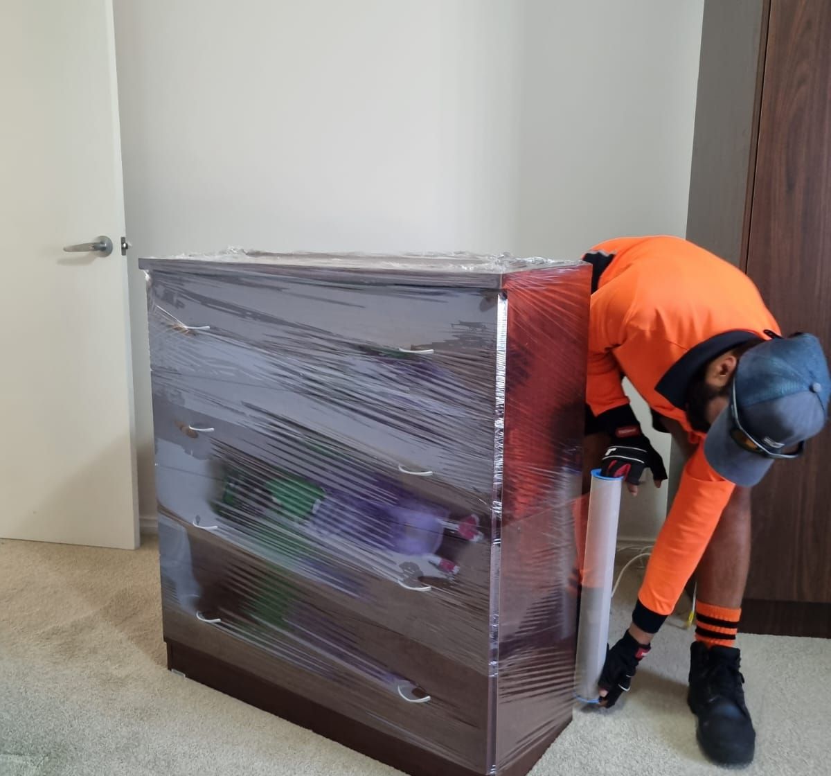 Removalist moving a shrink wrapped chest of drawers