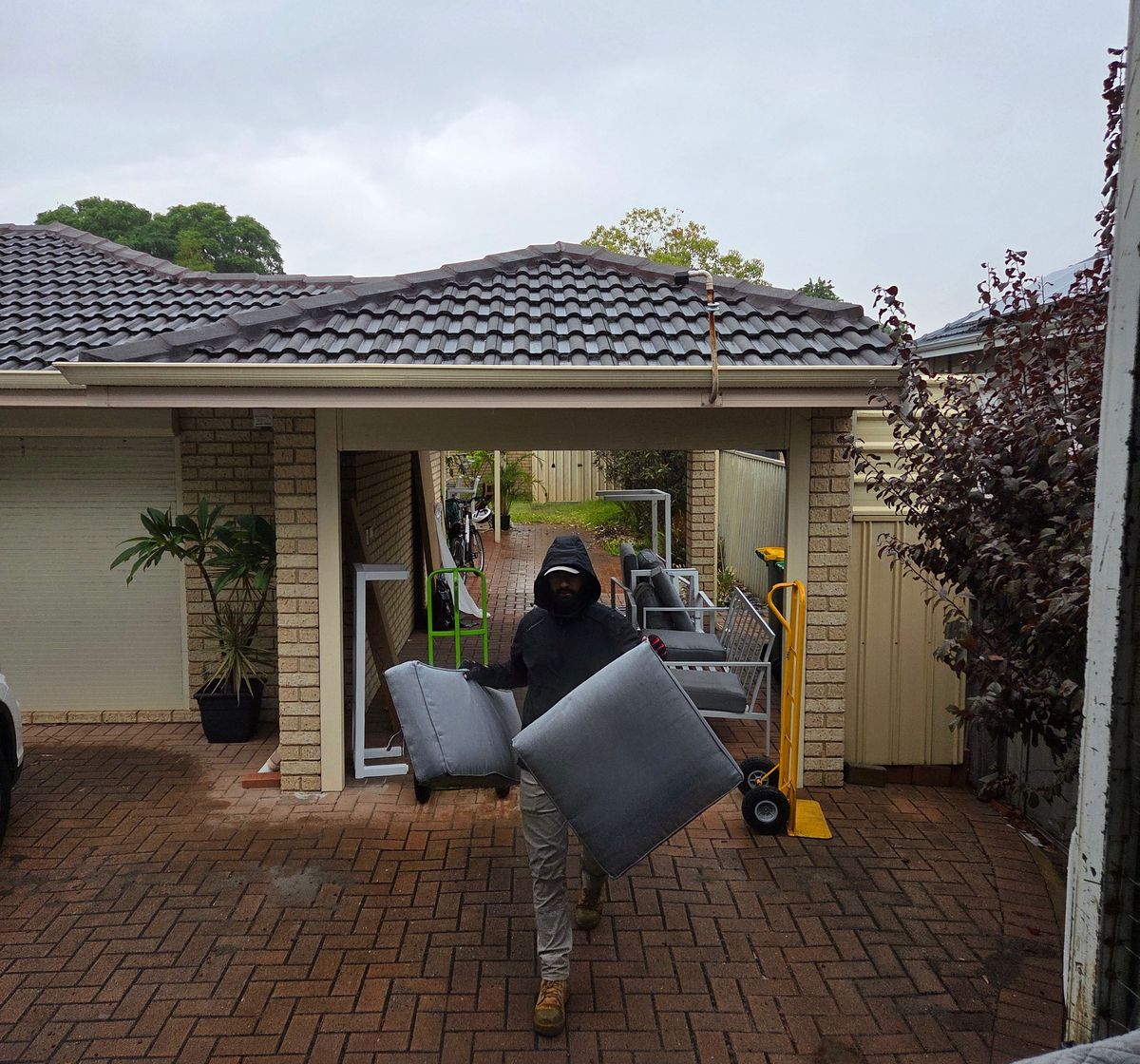 Removalist carrying an armchair across a brick courtyard