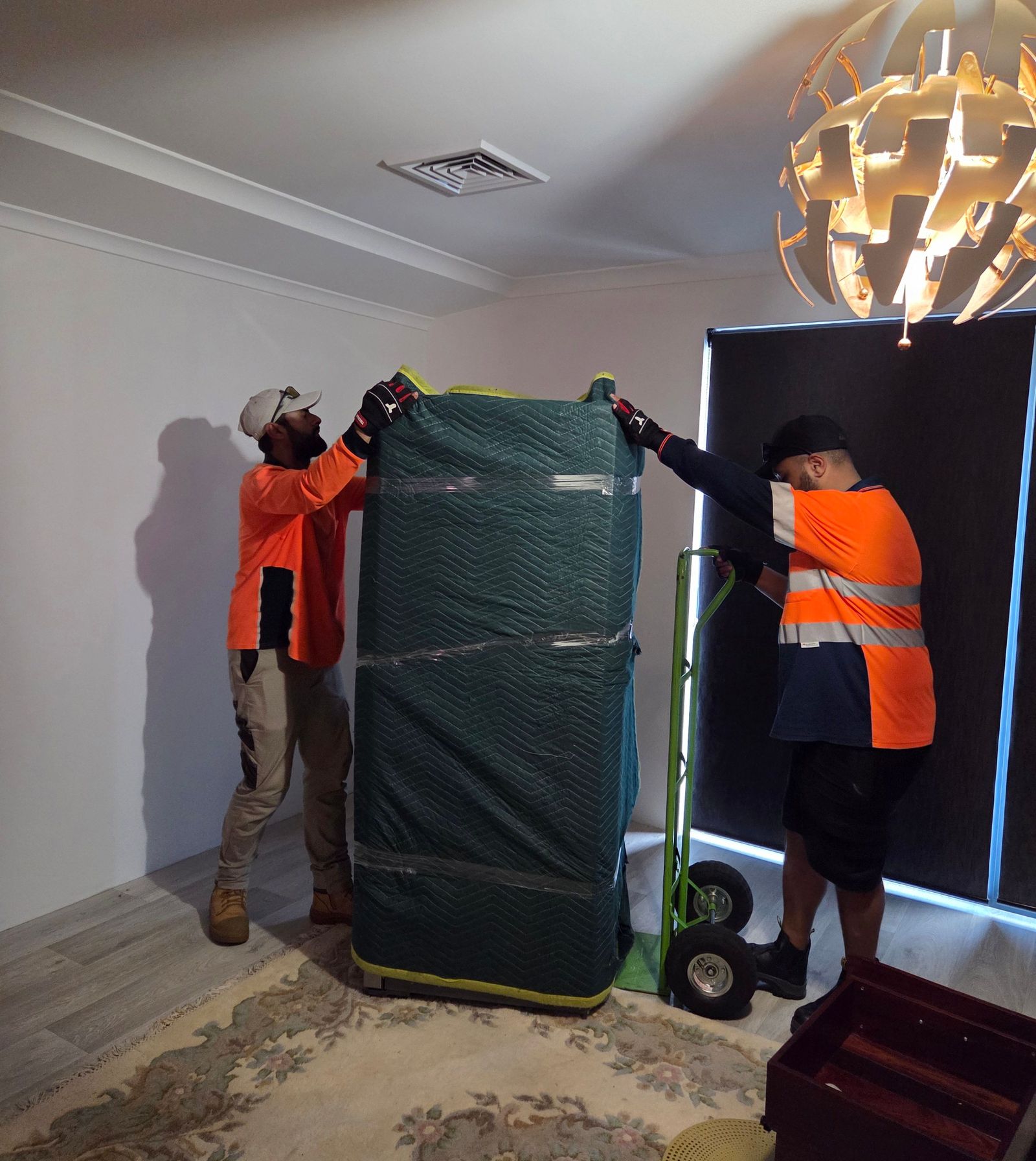 Two removalists in hi-vis moving a wrapped wardrobe out of a Perth bedroom